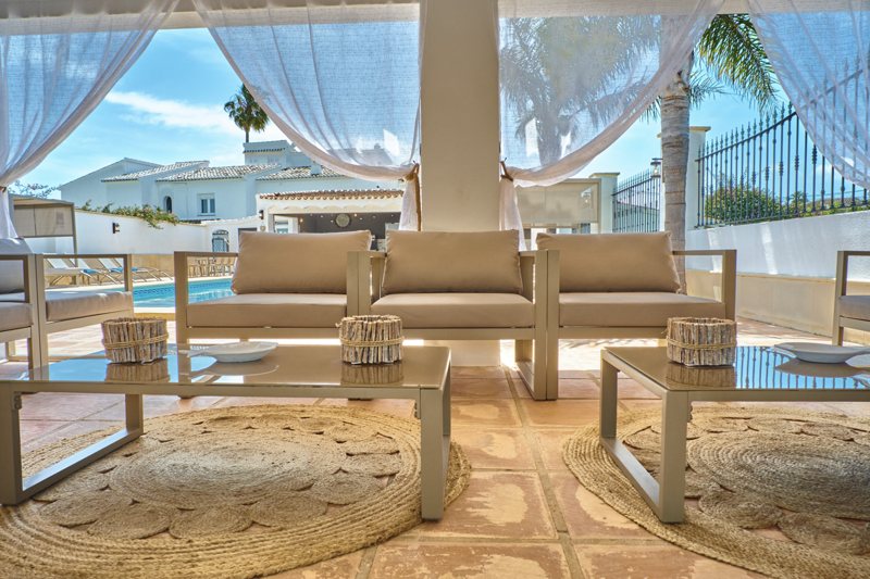 Überdachte Lounge mit weißen Vorhängen und Blick auf den Pool
