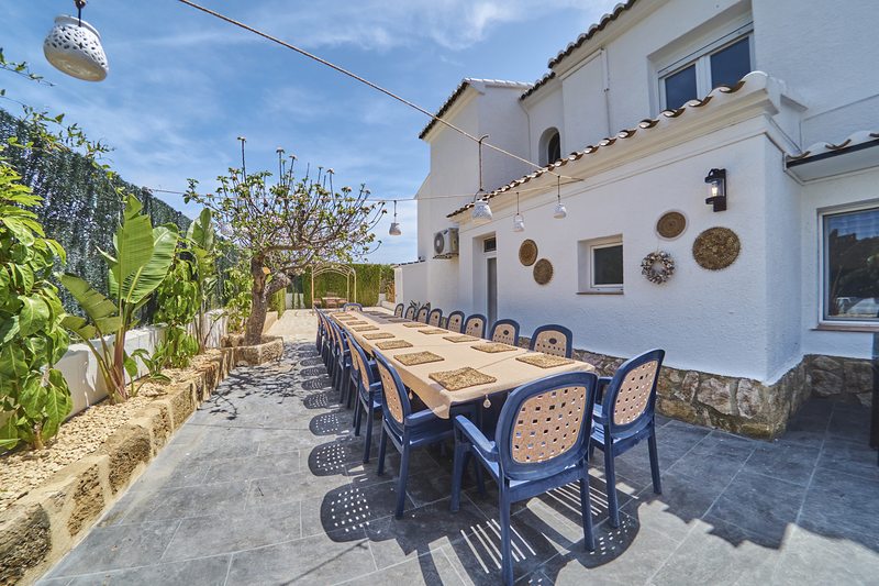 Mesa larga exterior con sillas azules junto a la pared blanca de la villa en Jávea, lista para una Navidad en familia al sol de invierno