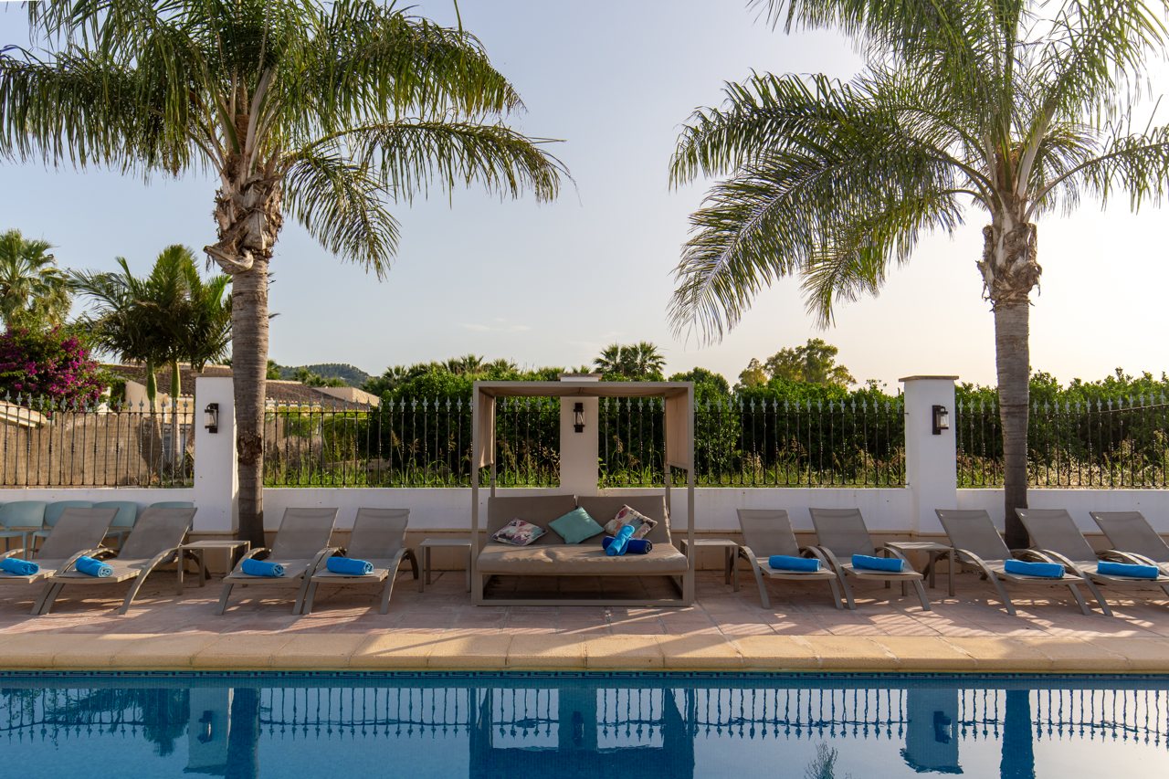 Reihe von Sonnenliegen am Pool zwischen den Palmen